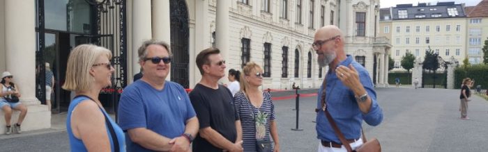 A guide speaks to visitors outside the palace.