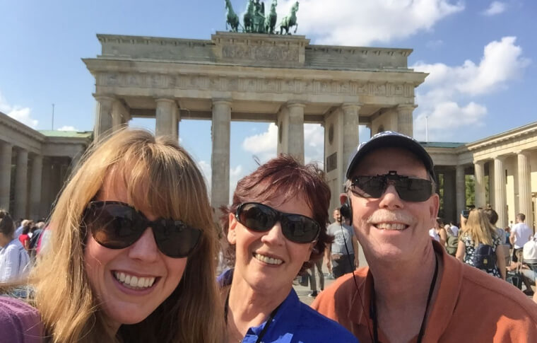 three people smiling in front of large memorial gate with statue on top