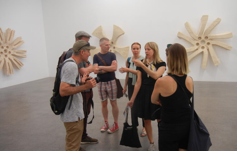 The group gather around a guide inside a gallery.