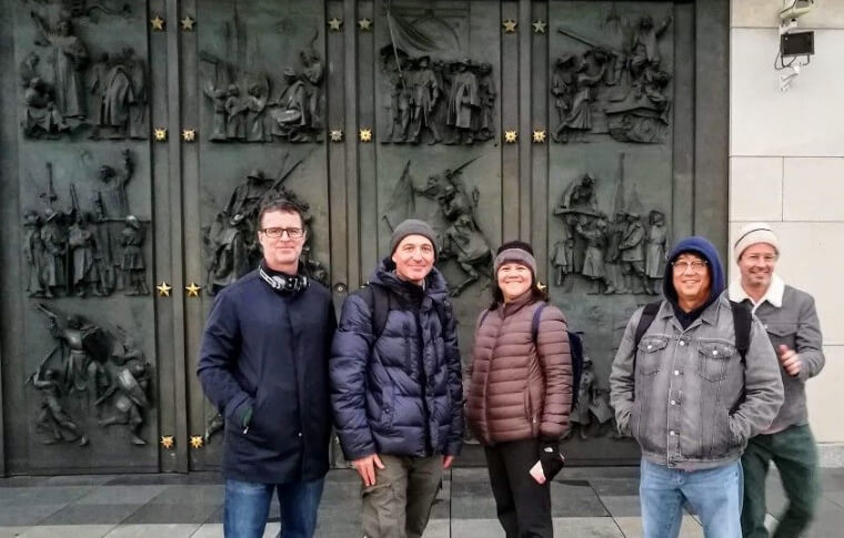 group of people smiling in front of large metal door with embossed figures