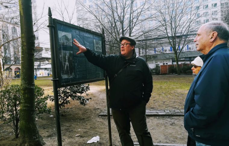 A guide points to a map and visitors watch.