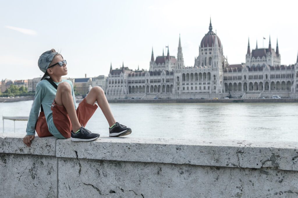 A boy looking out onto the Danube River in the center of Budapest with the Hungarian Parliament building in the background