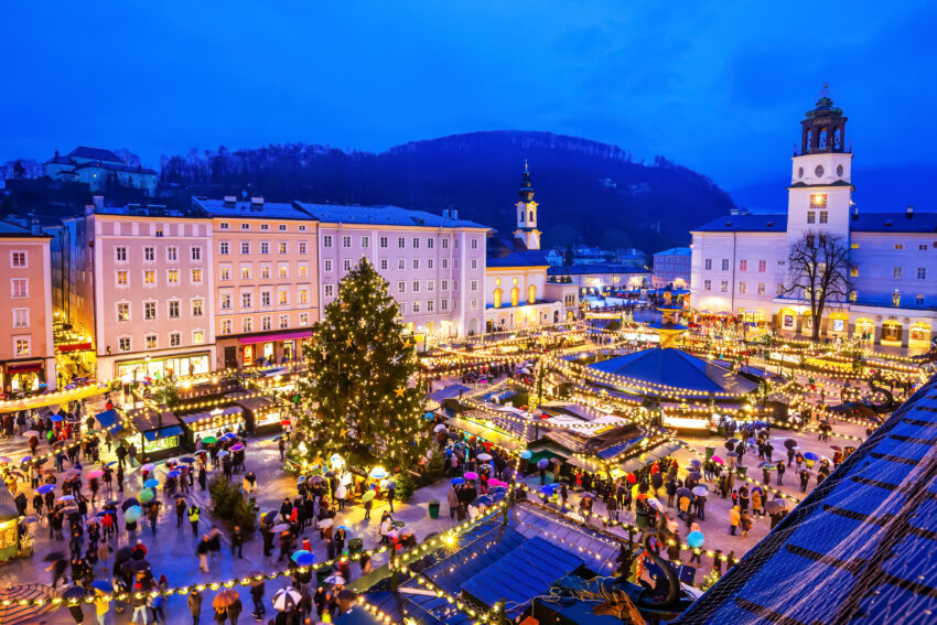 View of Salzburg's Christmas market in Old Town on an early winter evening, with bright yellow lights and a tree in the center.
